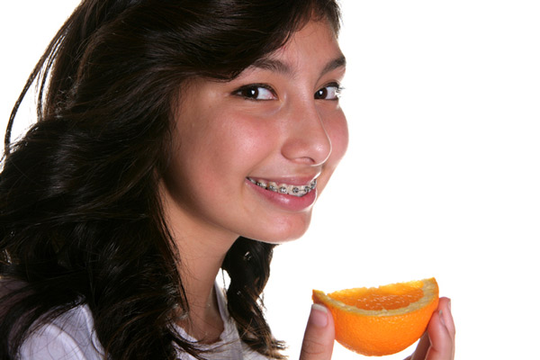Teenage girl with braces eating an orange slice after learning what foods to avoid at Lakewood Dental Arts in Lakewood, CA