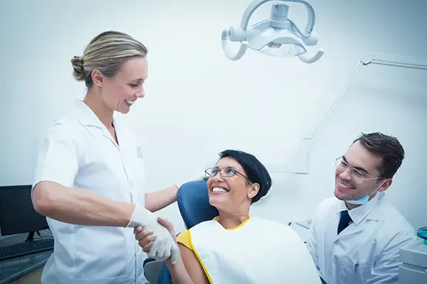A woman smiling and shaking hands with her dentist and a dental hygienist to the side at Lakewood Dental Arts in Lakewood, CA